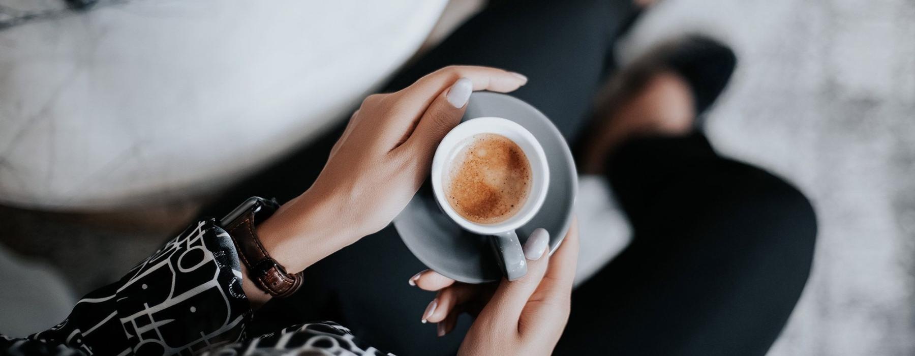 business woman sits next to a marble table with books and holds a saucer with a cup of espresso